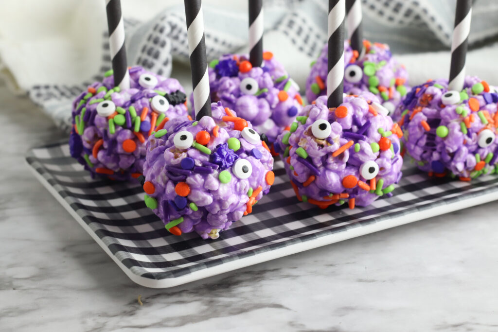 6 Creepy Halloween Popcorn Balls - purple colored popcorn balls with candy Halloween sprinkles and candy eyes - on a buffalo plaid plate