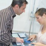 A man and woman standing in a bathroom shower stall while looking at samples of ceramic tile materials.