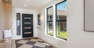 An entry way with a brown door, an area rug, two vertical windows, a small sitting area to the right and wall lights.