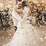A bride and groom dancing with each other on a dance floor at their wedding reception while confetti falls around them.