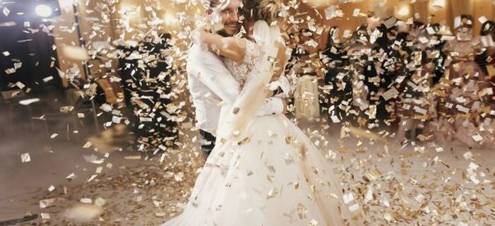 A bride and groom dancing with each other on a dance floor at their wedding reception while confetti falls around them.